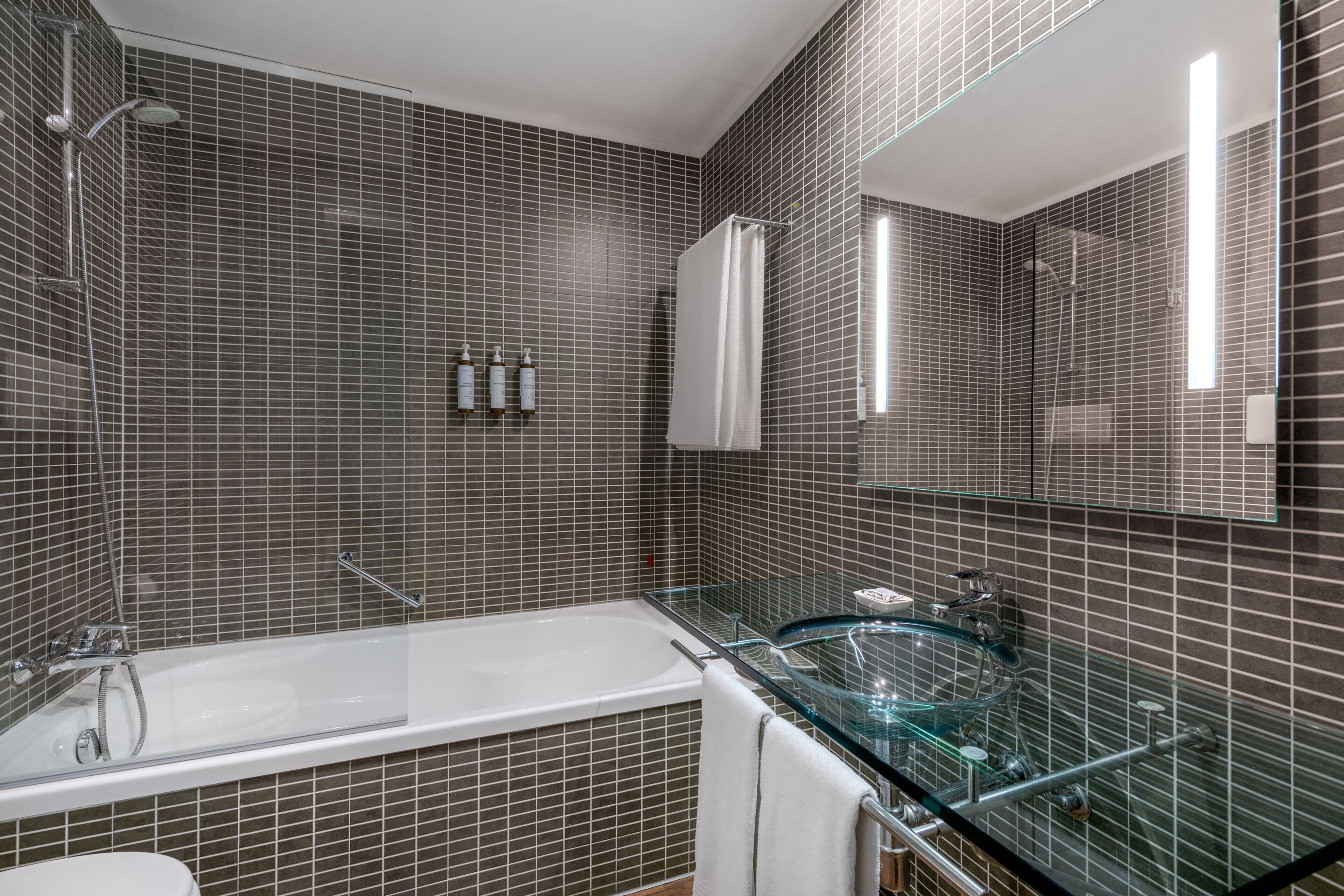 A modern bathroom with a glass-enclosed bathtub, a glass shower enclosure, and a large mirror.