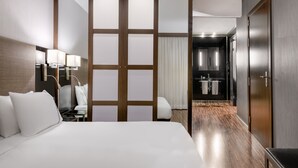 A hotel room with a large bed, a desk with a lamp, a sliding door leading to a bathroom, and a wooden floor. - AC Hotel Brescia by Marriott (Brescia)