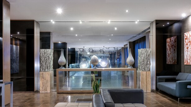 A modern lobby with a reception desk, seating area, and decorative vases. - AC Hotel Brescia by Marriott (Brescia)