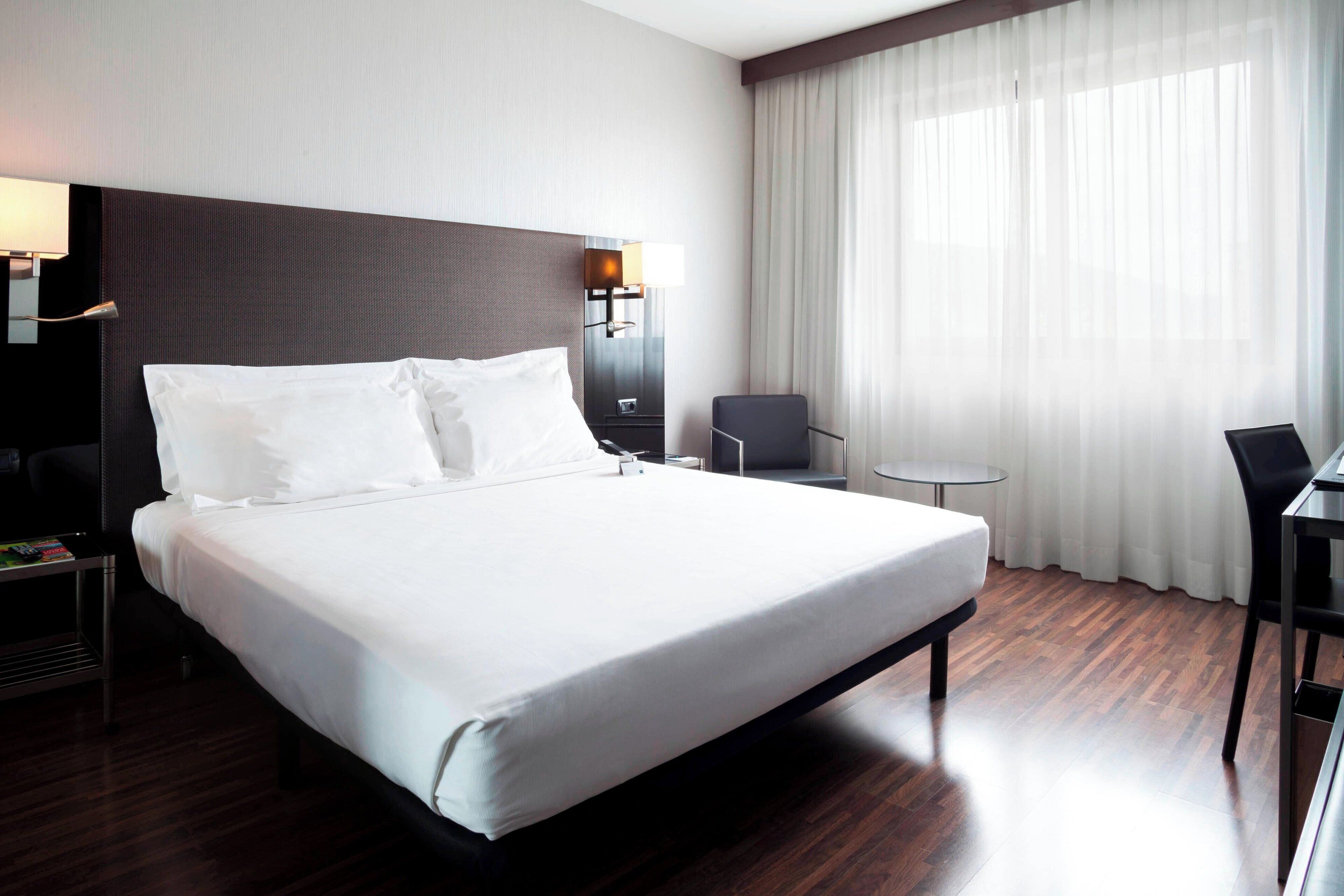 Una habitación de hotel moderna con una cama grande, un escritorio, una silla y una mesita.