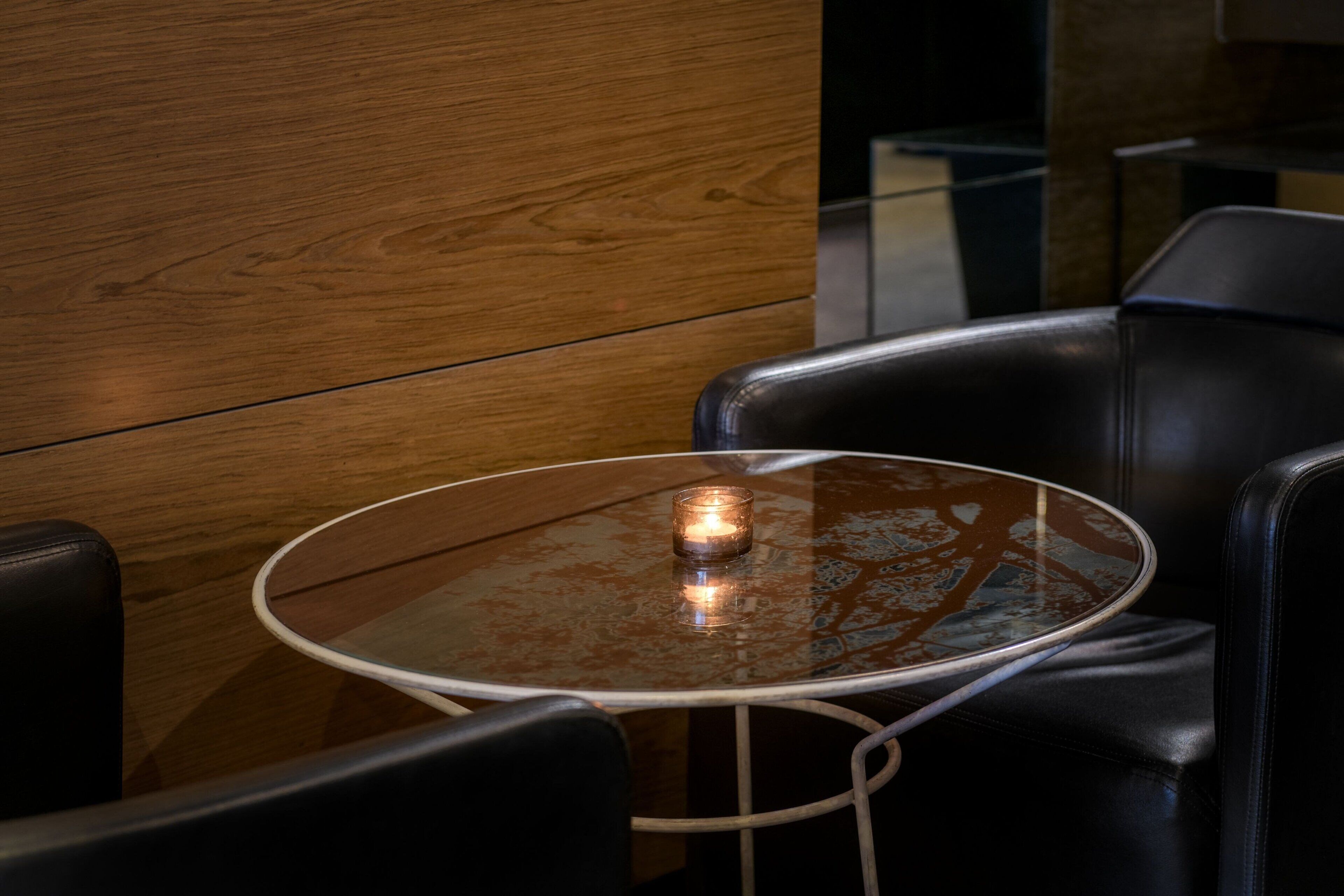 A round glass table with a metal frame, surrounded by black leather chairs.