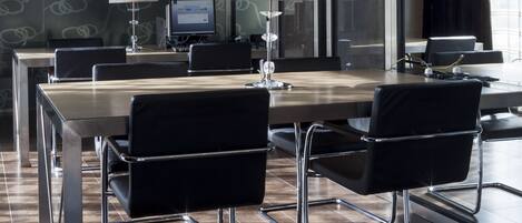 Uma sala de conferências moderna com uma mesa comprida, cadeiras pretas e duas luminárias.