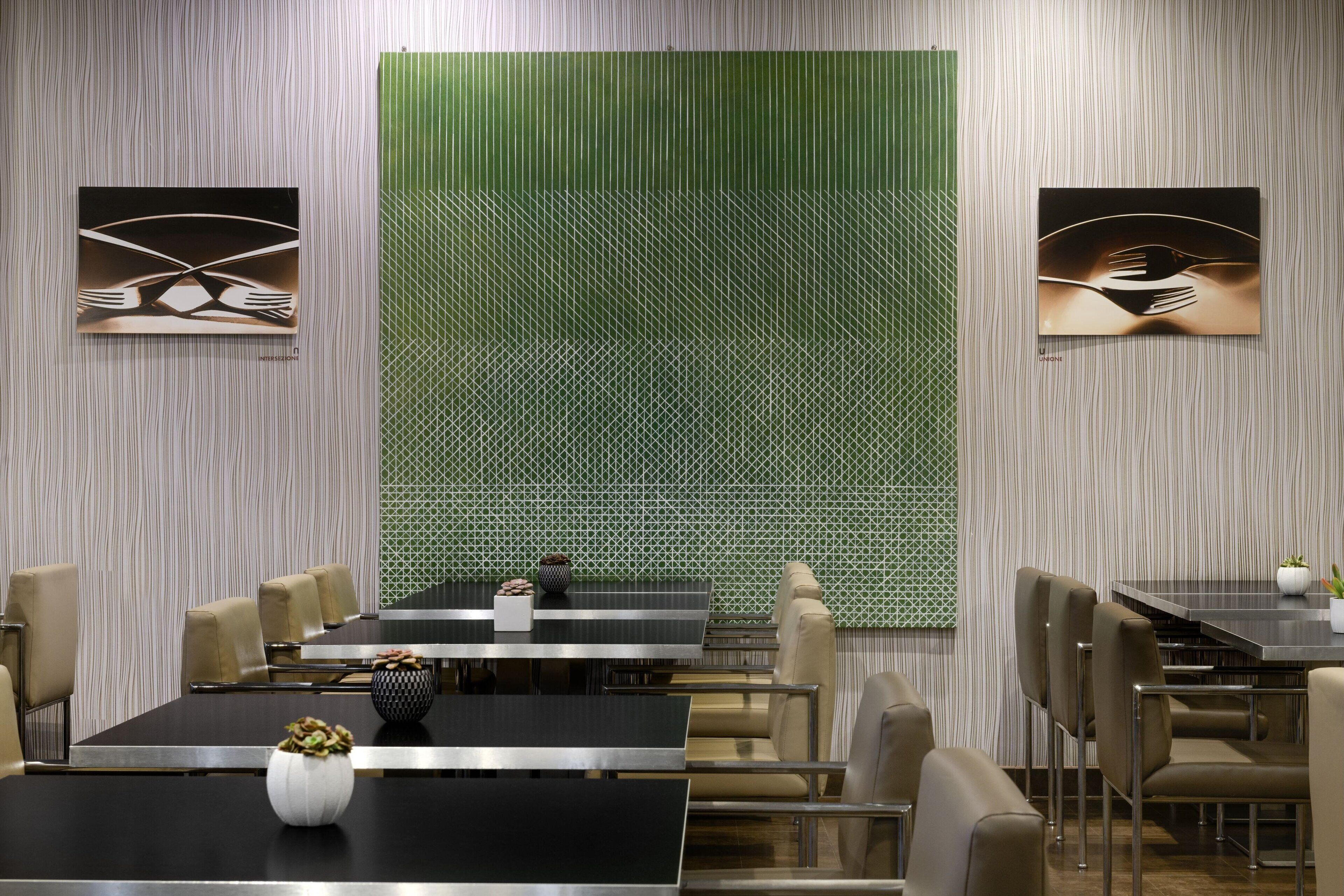 A modern dining area with a large table and chairs, a decorative wall with a geometric pattern, and two framed artworks.