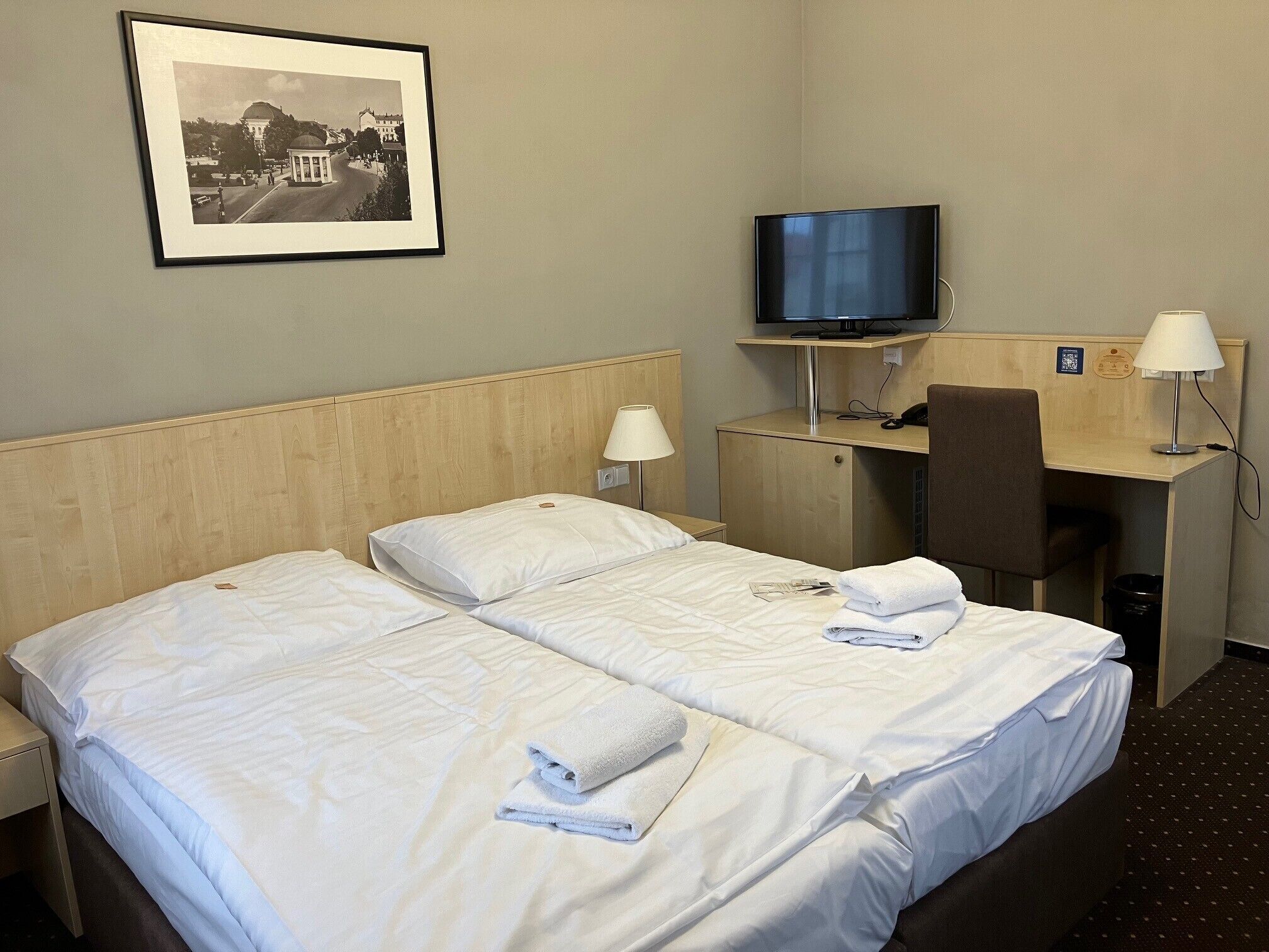 A hotel room with two beds, a desk, a chair, a television, and a framed picture on the wall.
