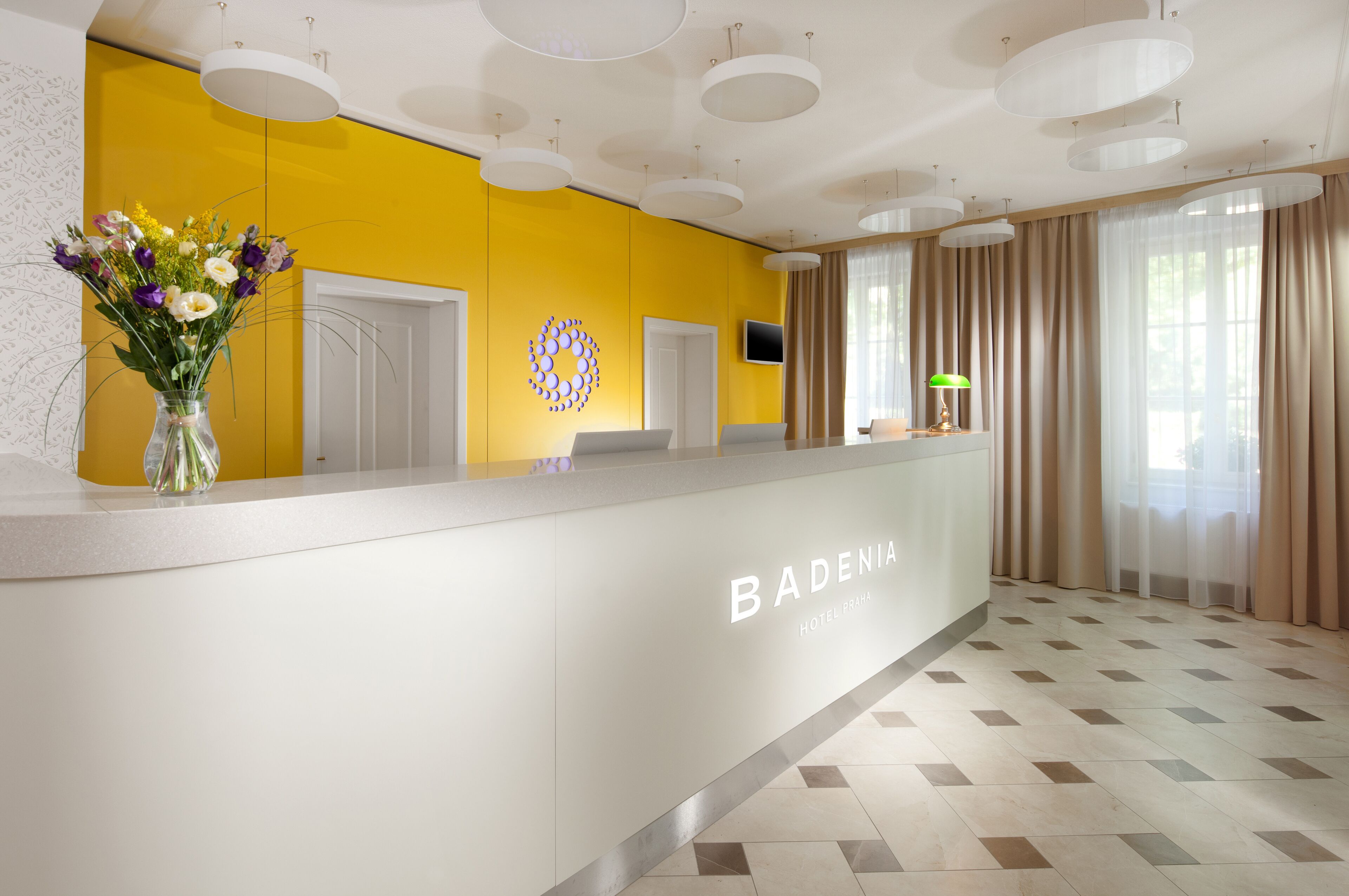 Un espace d’accueil au design moderne, comprenant un comptoir de réception, un vase de fleurs et un grand mur jaune.