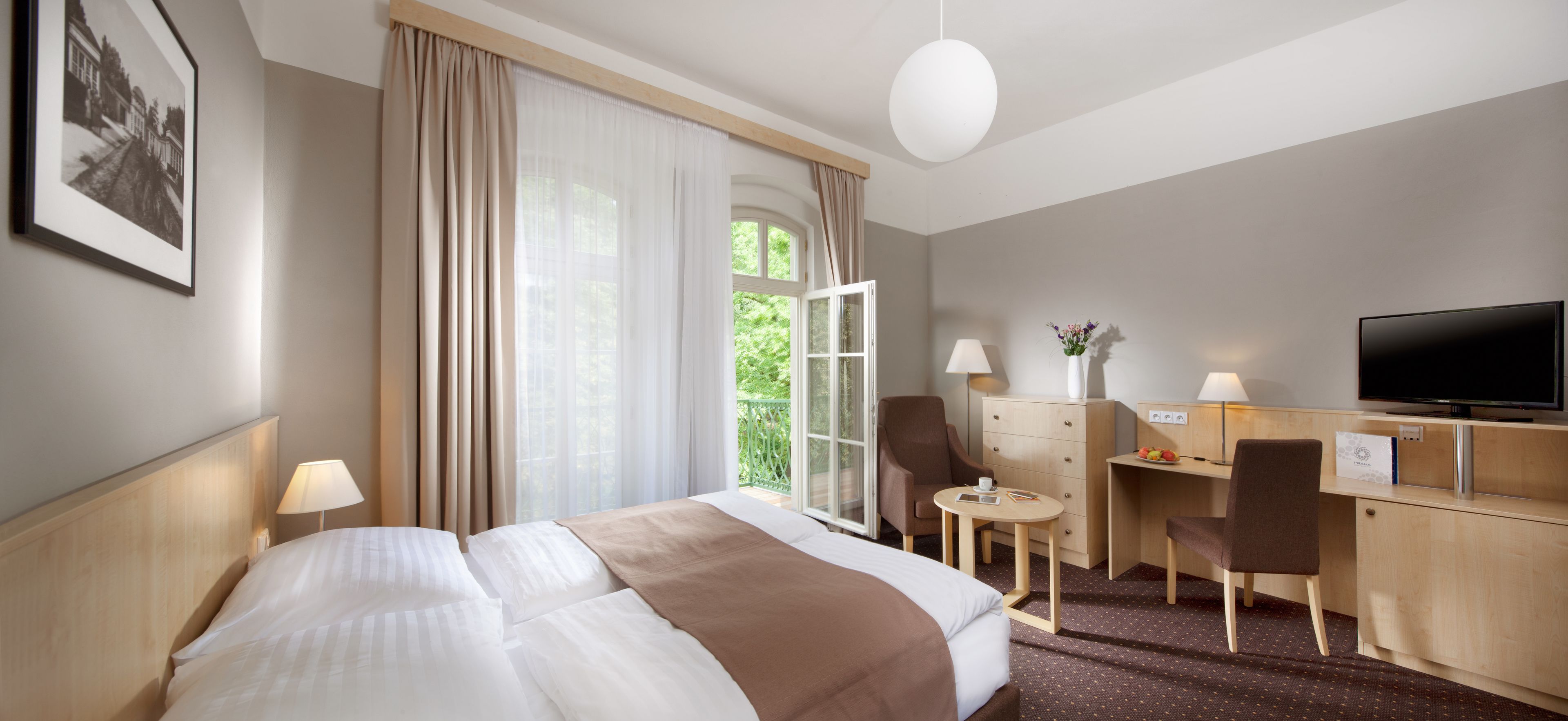 Hotellihuone, jossa on suuri sänky, työpöytä tuolilla, televisio ja ikkuna, jossa on verhot.