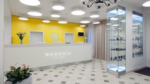 A reception area with a bright yellow wall, a chandelier, and a glass display case. - Badenia Hotel Praha (Frantiskovy Lazne)