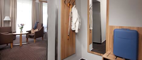 A hotel room with a seating area, a coat rack, a mirror, and a suitcase.