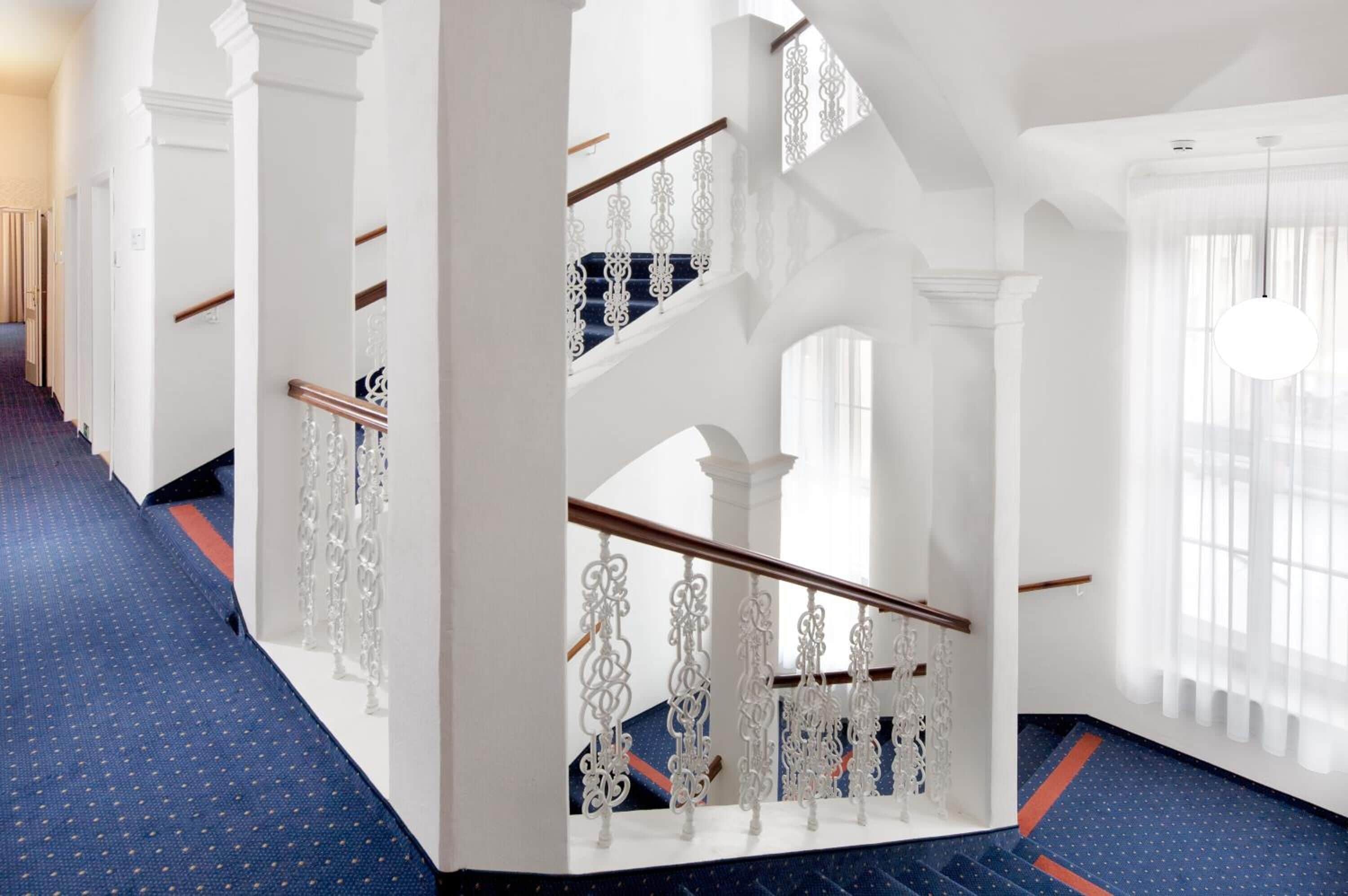 Un'imponente scala con ringhiere bianche decorate e gradini rivestiti di tappeto blu.
