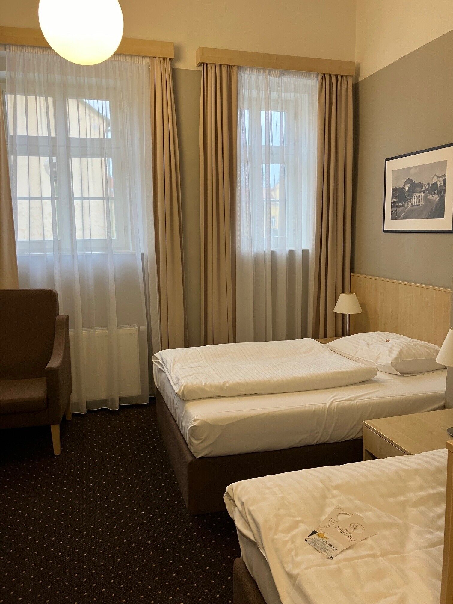 A hotel room with two beds, a chair, a lamp, and a framed picture on the wall.