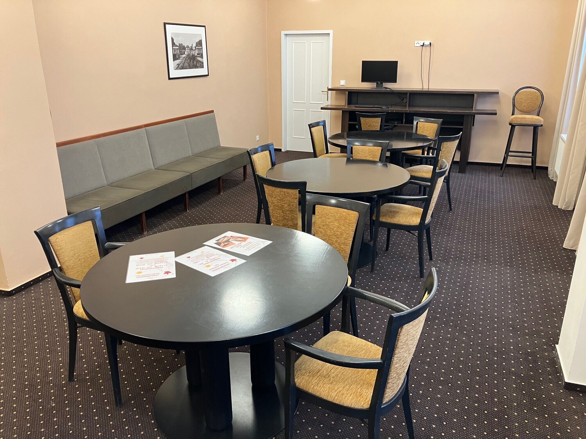 A conference room with round tables and chairs, a sofa, a TV on a stand, and a door.