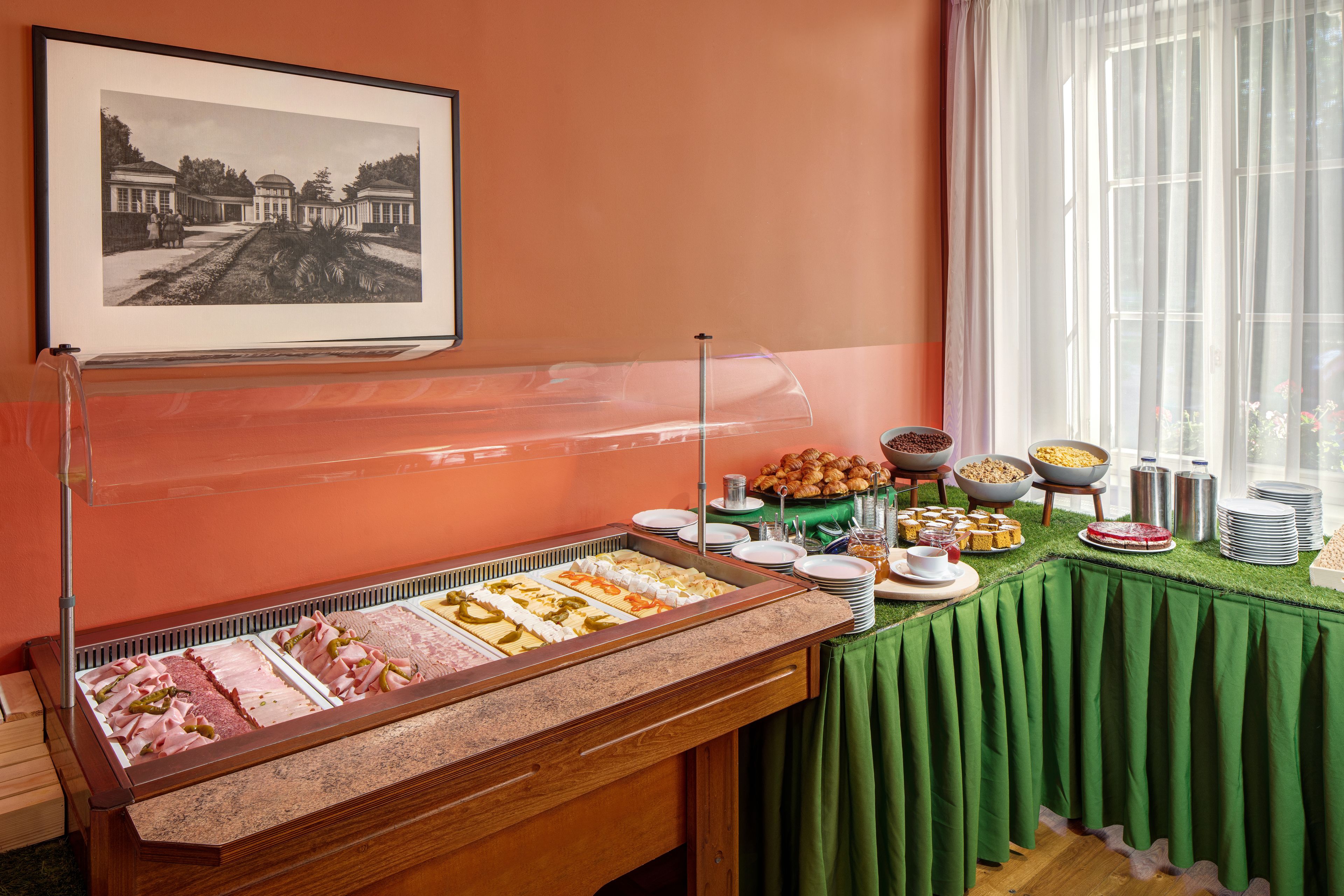 A buffet area with various food options, a framed historical photo on the wall, and a window with sheer curtains.
