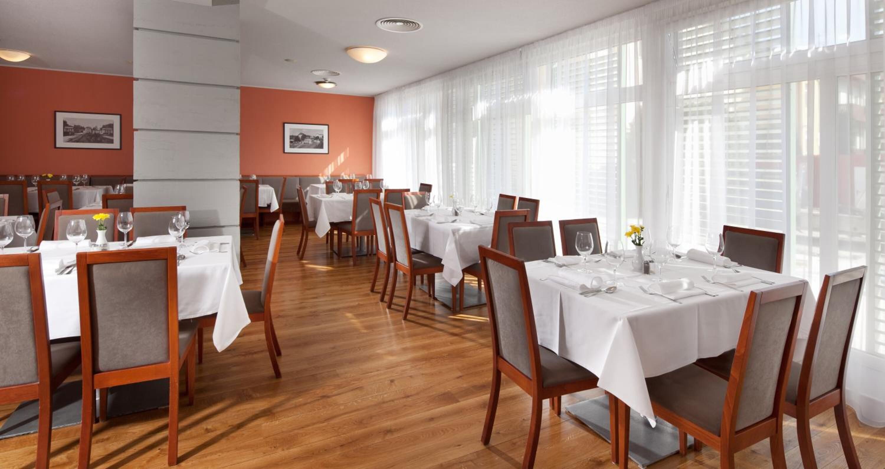 Un restaurante con varias mesas dispuestas para comer, con sillas de madera y manteles blancos.