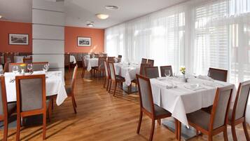A restaurant with multiple tables set for dining, featuring wooden chairs and white tablecloths.