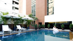 A swimming pool with lounge chairs and umbrellas, surrounded by potted plants and a building facade. - FuramaXclusive Sukhumvit (Bangkok)