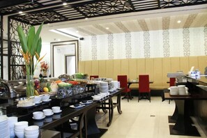 A buffet setup with various food items and dishes, a seating area with chairs, and a decorative wall with a patterned design. - FuramaXclusive Sukhumvit (Bangkok)