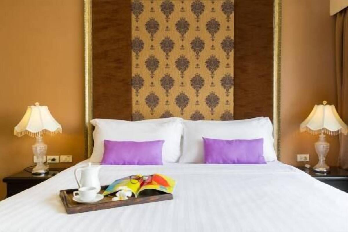 A hotel room with a large bed, two nightstands, a tray with a book and glasses, and a patterned wallpaper.