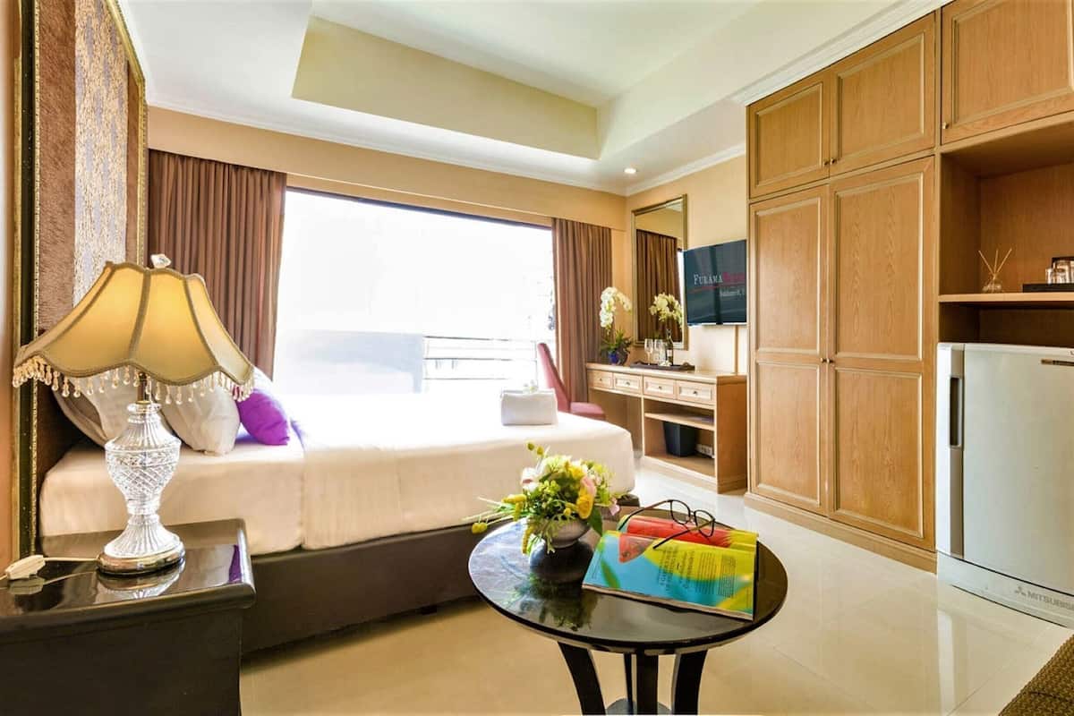 A hotel room with a bed, a desk, a refrigerator, and a window with curtains.