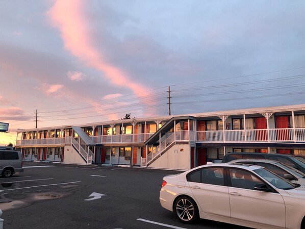 A motel with multiple floors, a central staircase, and a parking lot with cars. - New Sea Breeze Motel (Pleasantville)