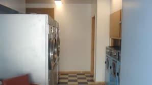 A compact kitchen with a refrigerator, washing machine, and a chair. - New Sea Breeze Motel (Pleasantville)