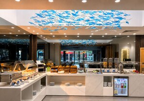 A modern hotel lobby with a central buffet area, a refrigerator, and a large ceiling mural of fish. - Eurotraveller Hotel Premier Tower Bridge (London)
