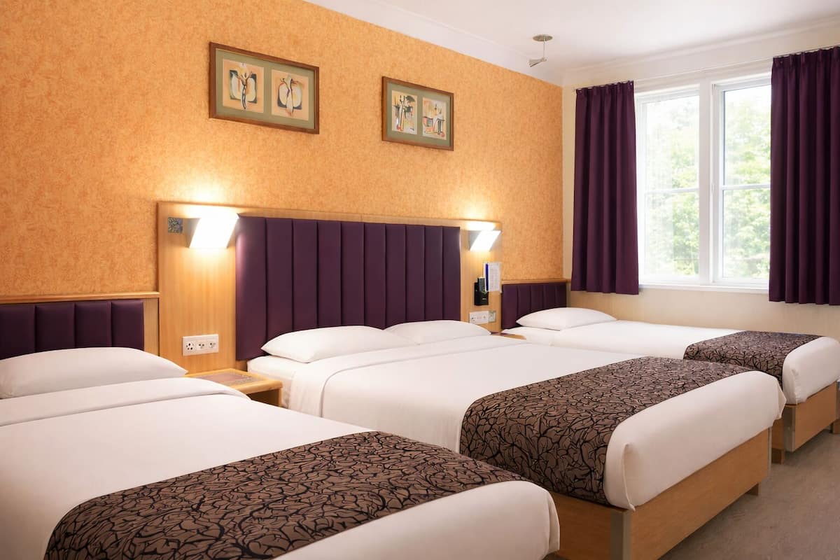 Ein Hotelzimmer mit drei Betten, einem Kopfteil mit integrierter Beleuchtung, einem Fenster mit violetten Vorhängen und Kunstwerken an der Wand.