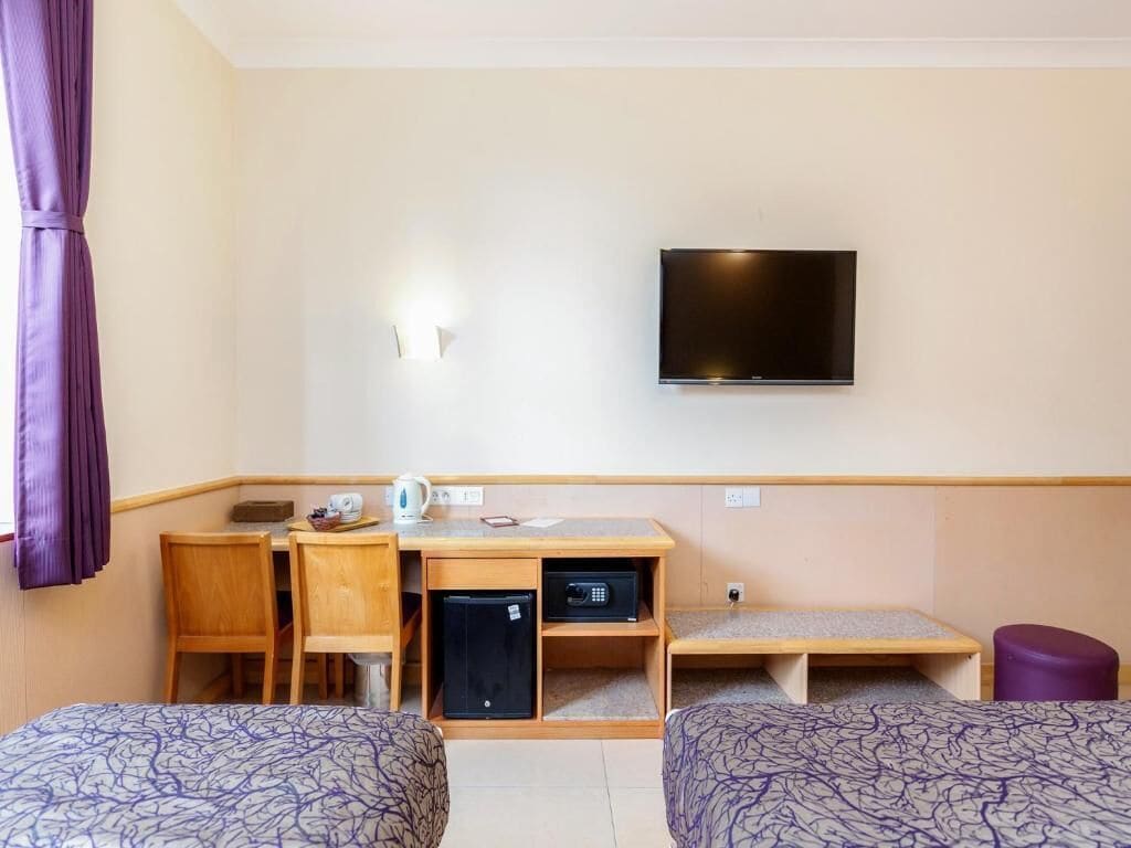 A hotel room with two beds, a desk with a computer, a television, and a small refrigerator.