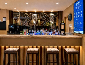 A bar area with a counter, stools, a digital menu board, and a clock. - Eurotraveller Hotel Premier Tower Bridge (London)