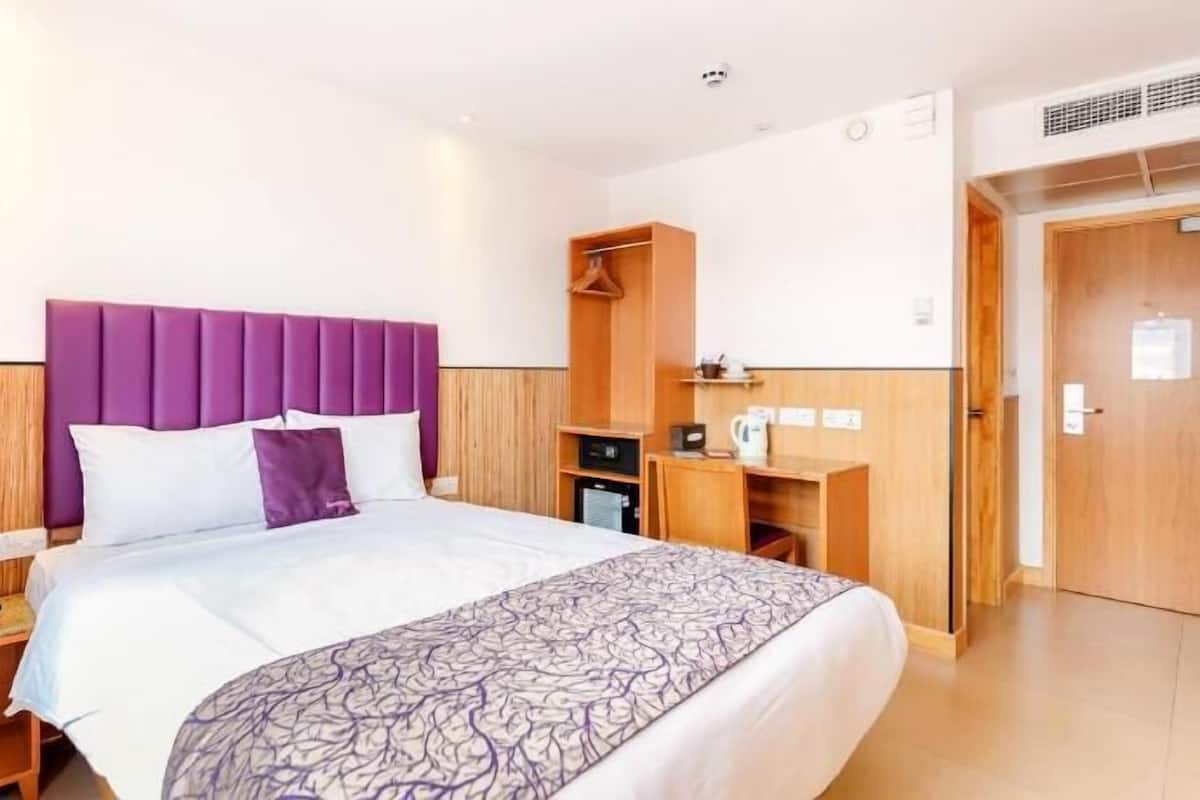 Ein Hotelzimmer mit Bett, Nachttisch, Schrank und Schreibtisch mit Stuhl.