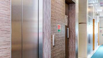 En moderne elevator med metaldoors og træpaneler, placeret i en gang med blå tæppe.