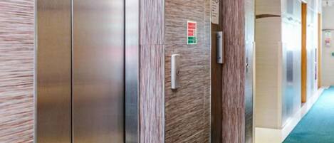 A modern elevator with metallic doors and a wooden panel design, located in a hallway with a blue carpet.