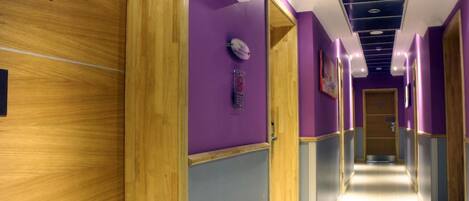 A hotel corridor with purple walls, wooden doors, and a ceiling with recessed lighting.