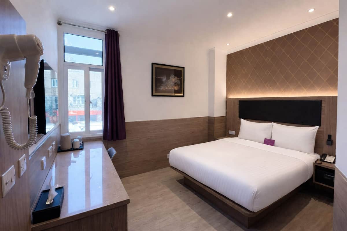 Ein Hotelzimmer mit Bett, Nachttisch, Spiegel, einem Fenster mit Vorhängen und einem Wandbild.