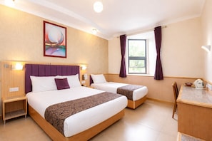 A hotel room with two beds, a desk, a chair, a window with curtains, a painting on the wall, and a nightstand with a lamp. - Eurotraveller Hotel Premier Tower Bridge (London)