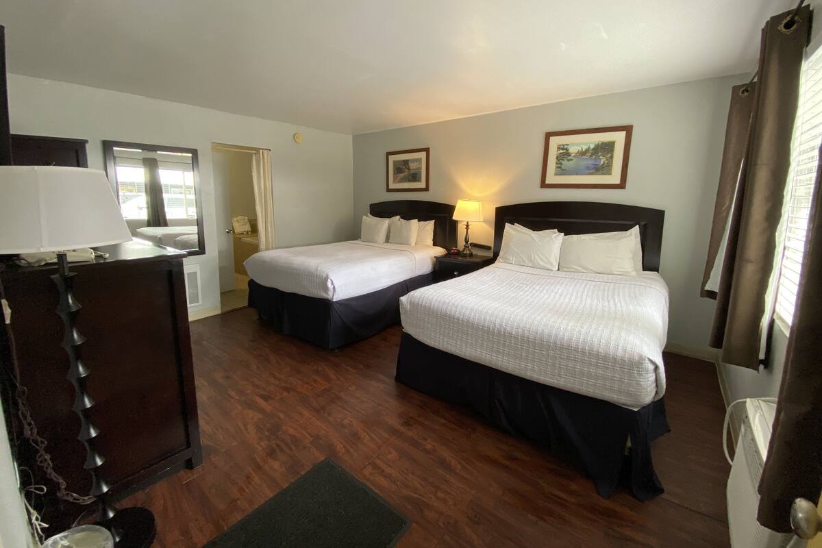 A hotel room with two beds, a desk with a lamp, a mirror, and a door leading to a bathroom.