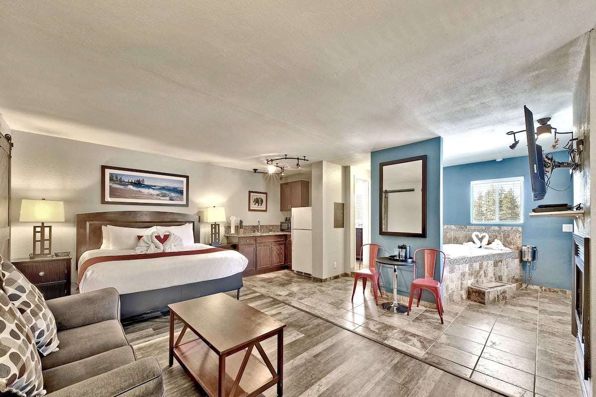 A hotel room with a bed, a desk, a chair, a bathroom with a bathtub, and a TV mounted on the wall.