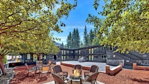 An outdoor seating area with a fire pit, surrounded by a patio with a view of a multi-story building. - Heavenly Inn (South Lake Tahoe)