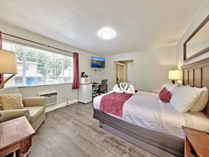 A hotel room with a bed, a desk, a chair, a TV, and a window with curtains. - Heavenly Inn (South Lake Tahoe)