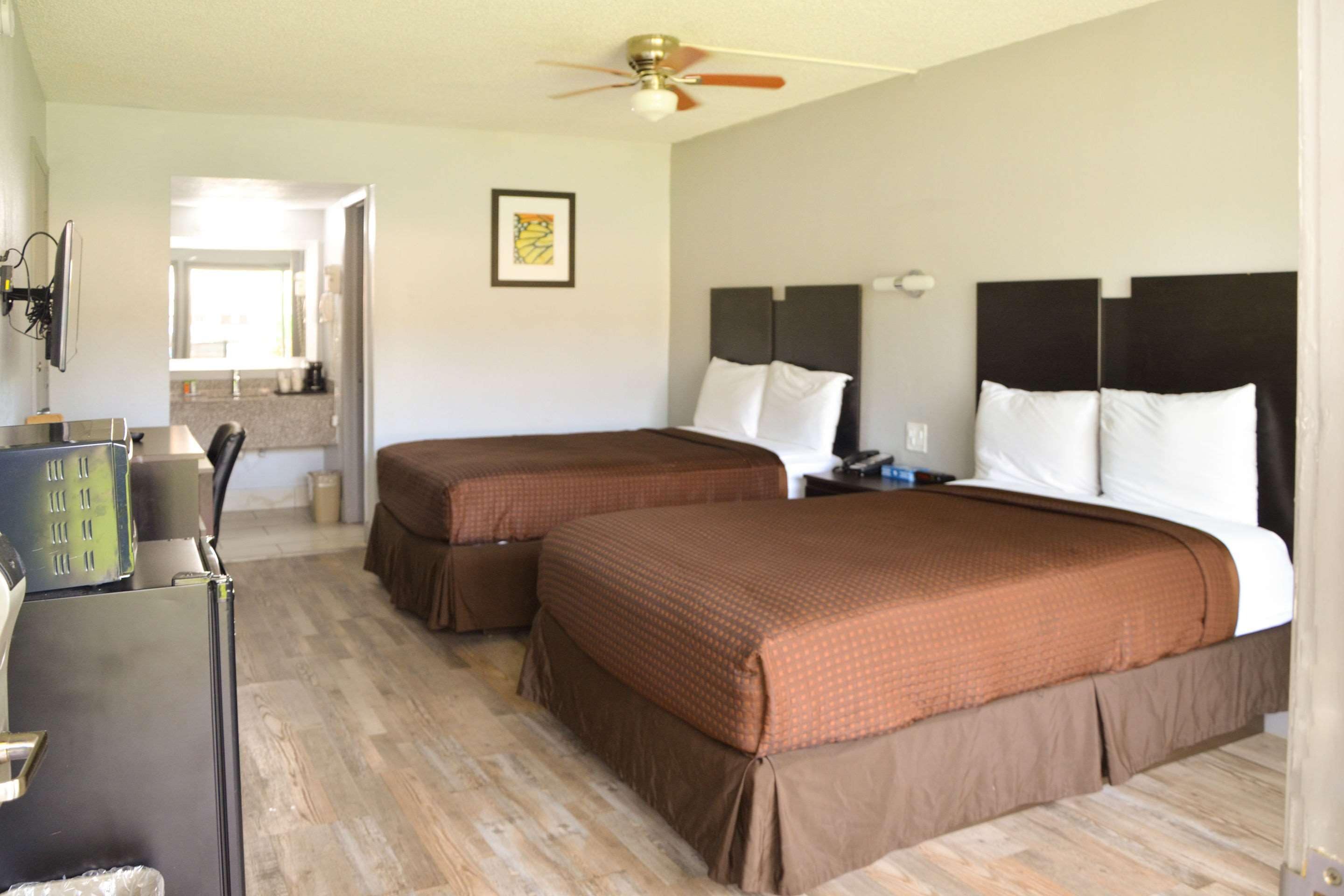 A hotel room with two beds, a desk, a ceiling fan, and a bathroom visible in the background.