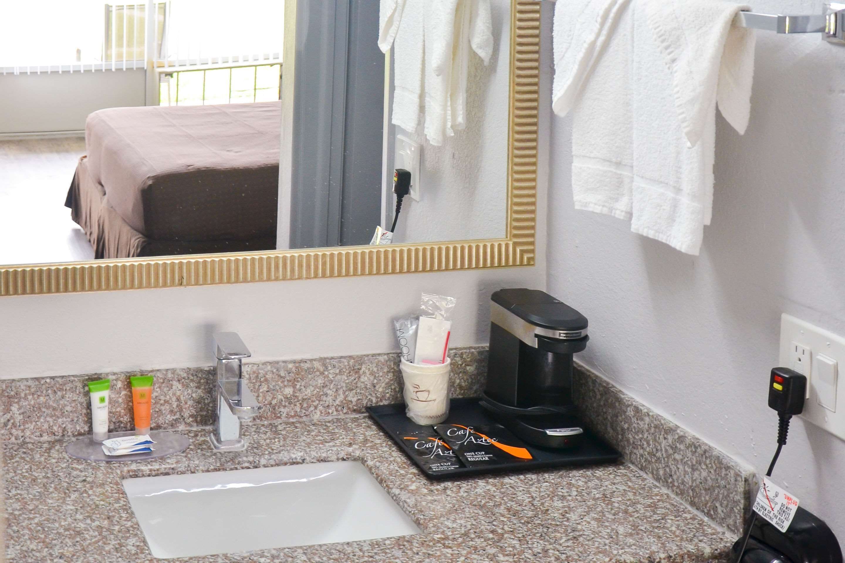 A hotel bathroom with a sink, mirror, toiletries, and a coffee maker.