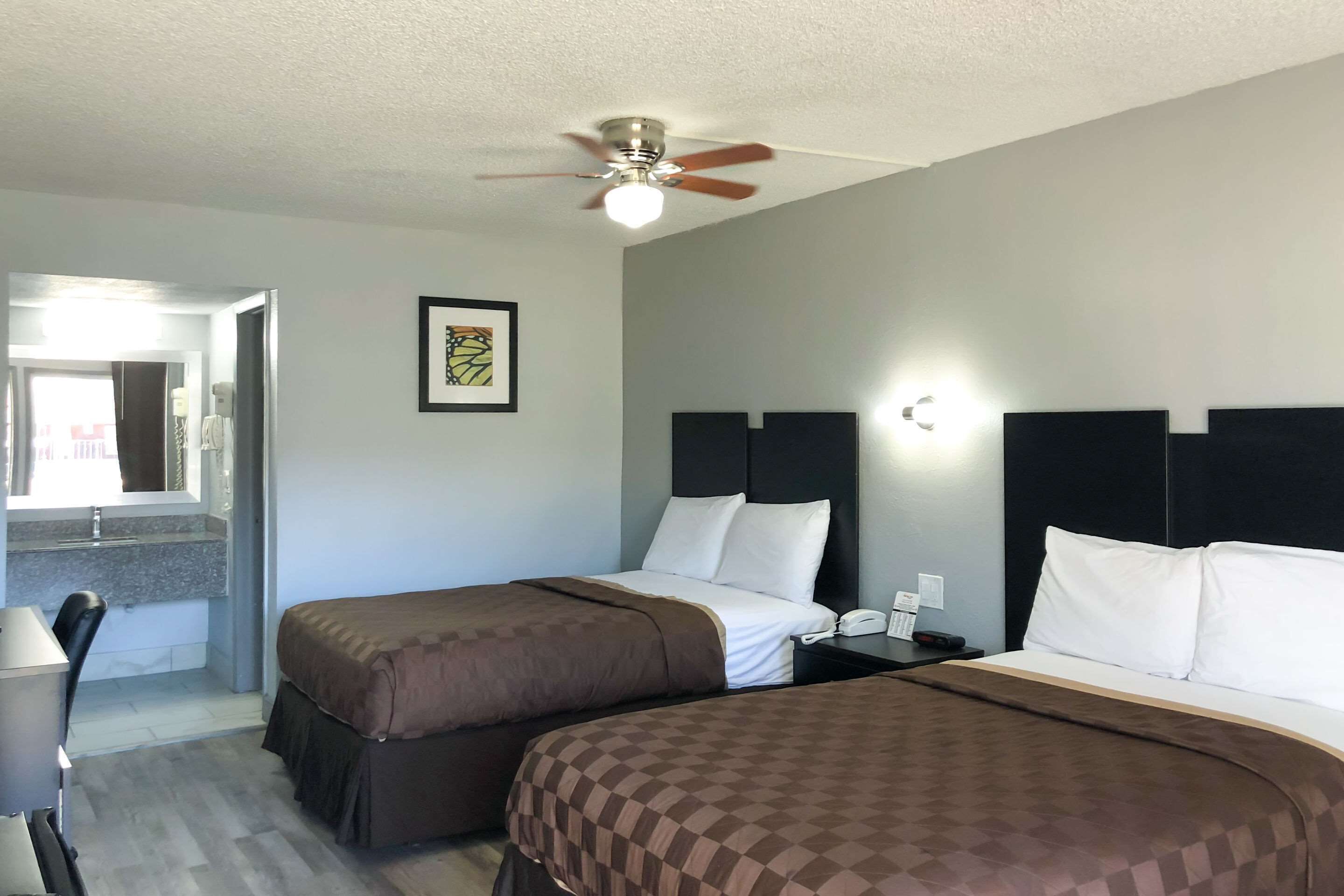 A hotel room with two beds, a ceiling fan, a desk with a chair, and a bathroom visible through an open door.