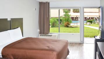 A hotel room with a bed, a desk, and a view of a swimming pool and greenery.