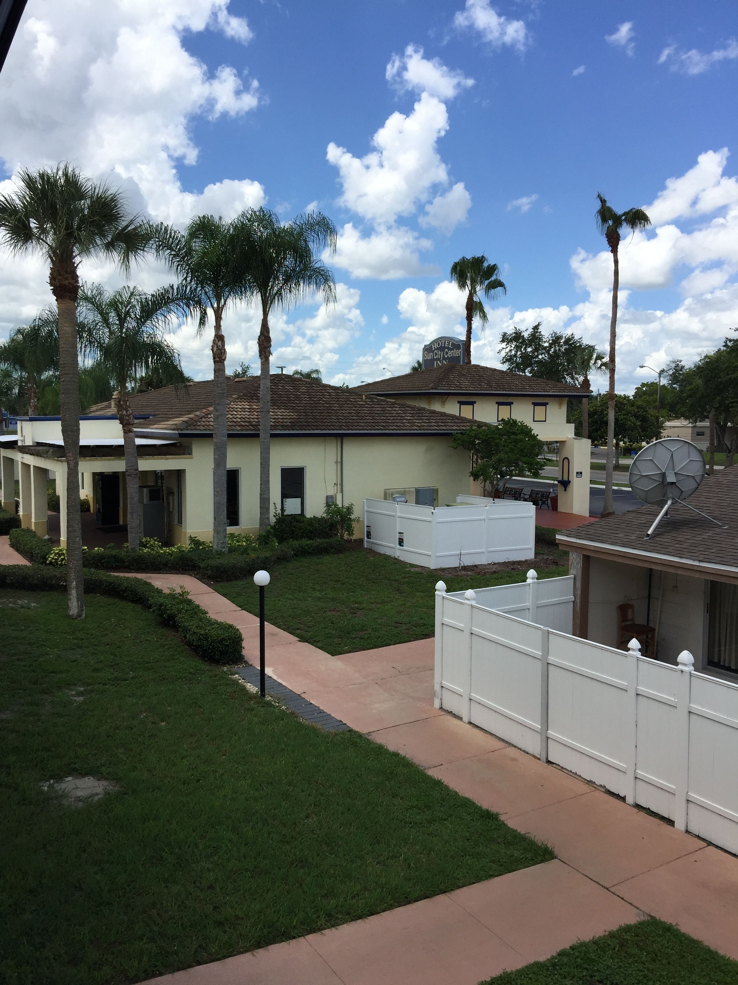 A hotel with a flat roof, a fenced yard, and palm trees.