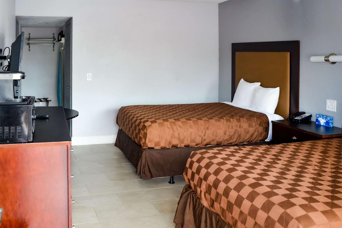 A hotel room with two beds, a desk with a coffee machine, and a small kitchenette.