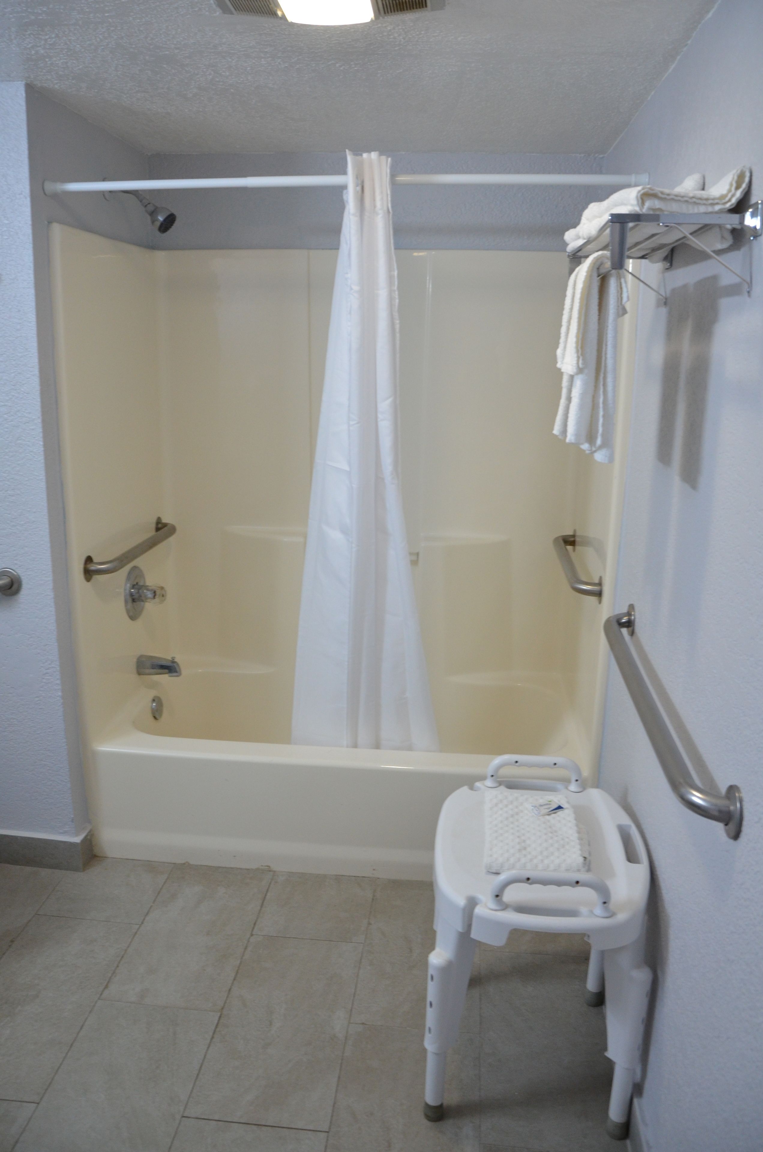 Un baño con bañera, cortina de ducha, barra de apoyo, taburete y toallero.