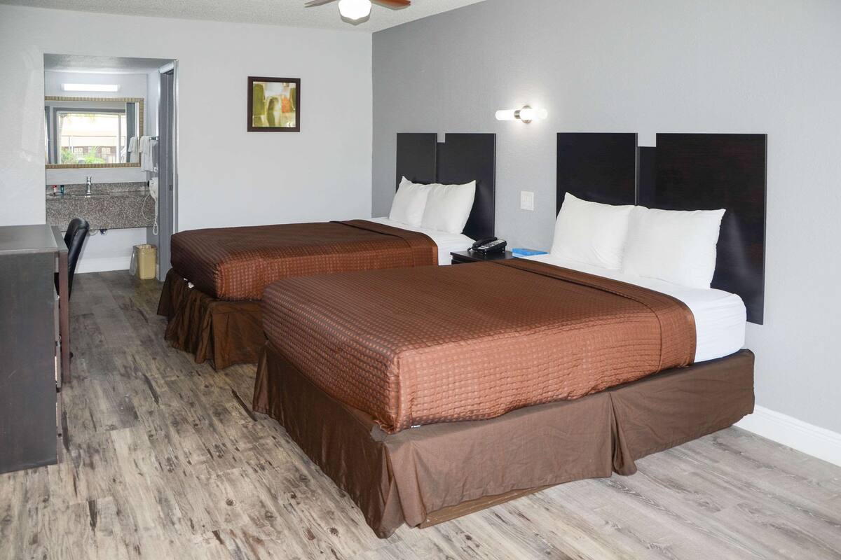 A hotel room with two beds, a desk, and a bathroom visible through an open door.