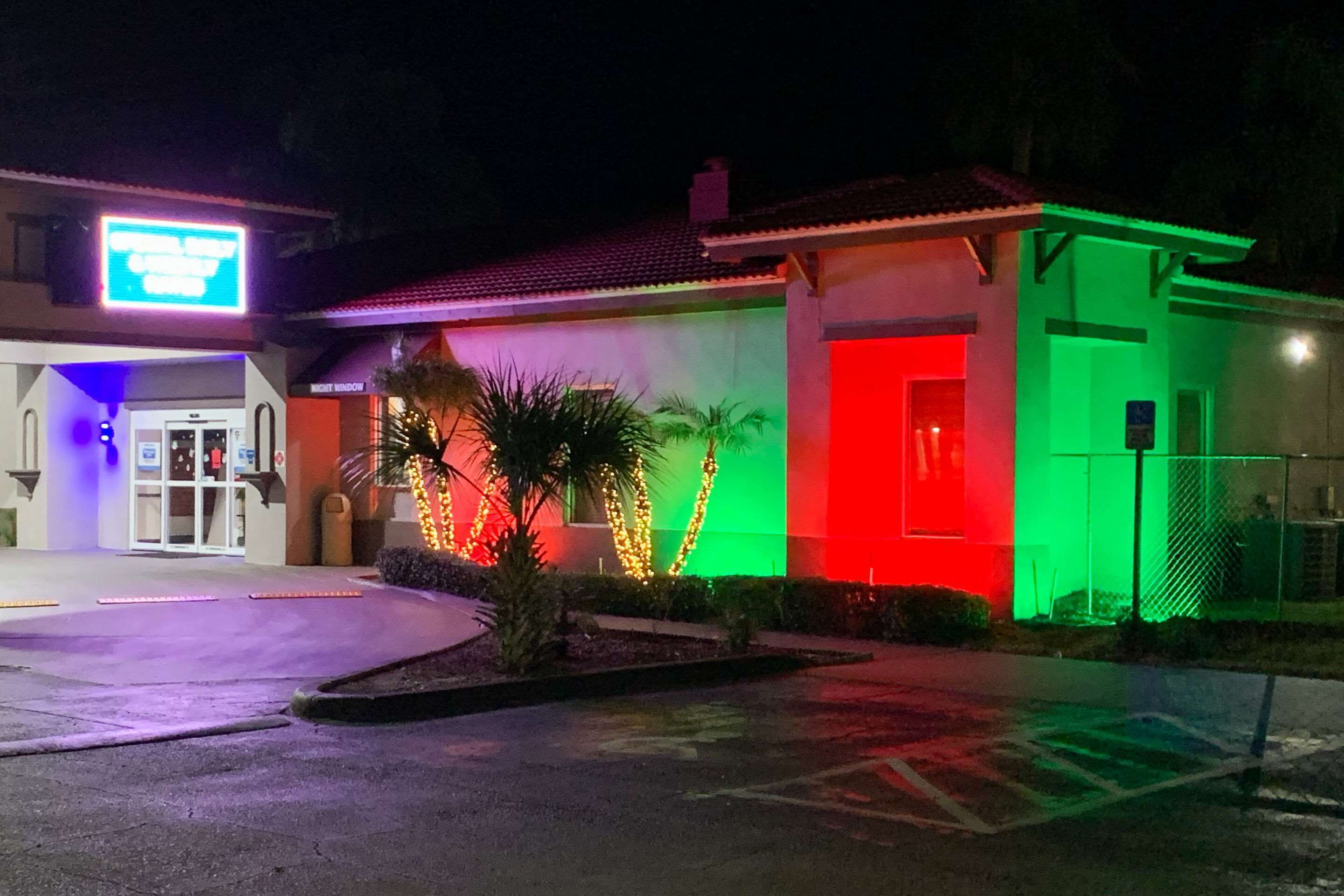 A building with a brightly lit entrance, palm trees, and a sign that reads "OPEN 24 HOURS."
