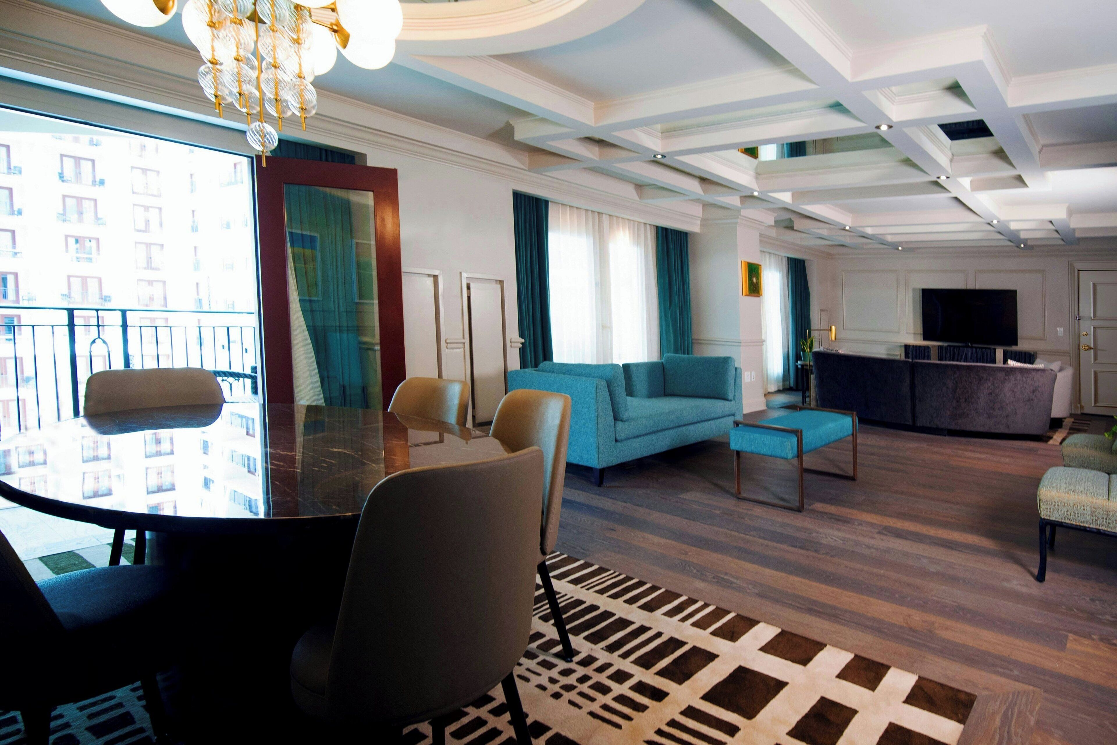 Habitación de hotel moderna con comedor, sofá, televisión y balcón con vistas a la ciudad.