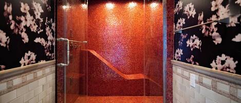 A glass-enclosed shower with a tiled floor and walls, a metal showerhead, and a visible drain.