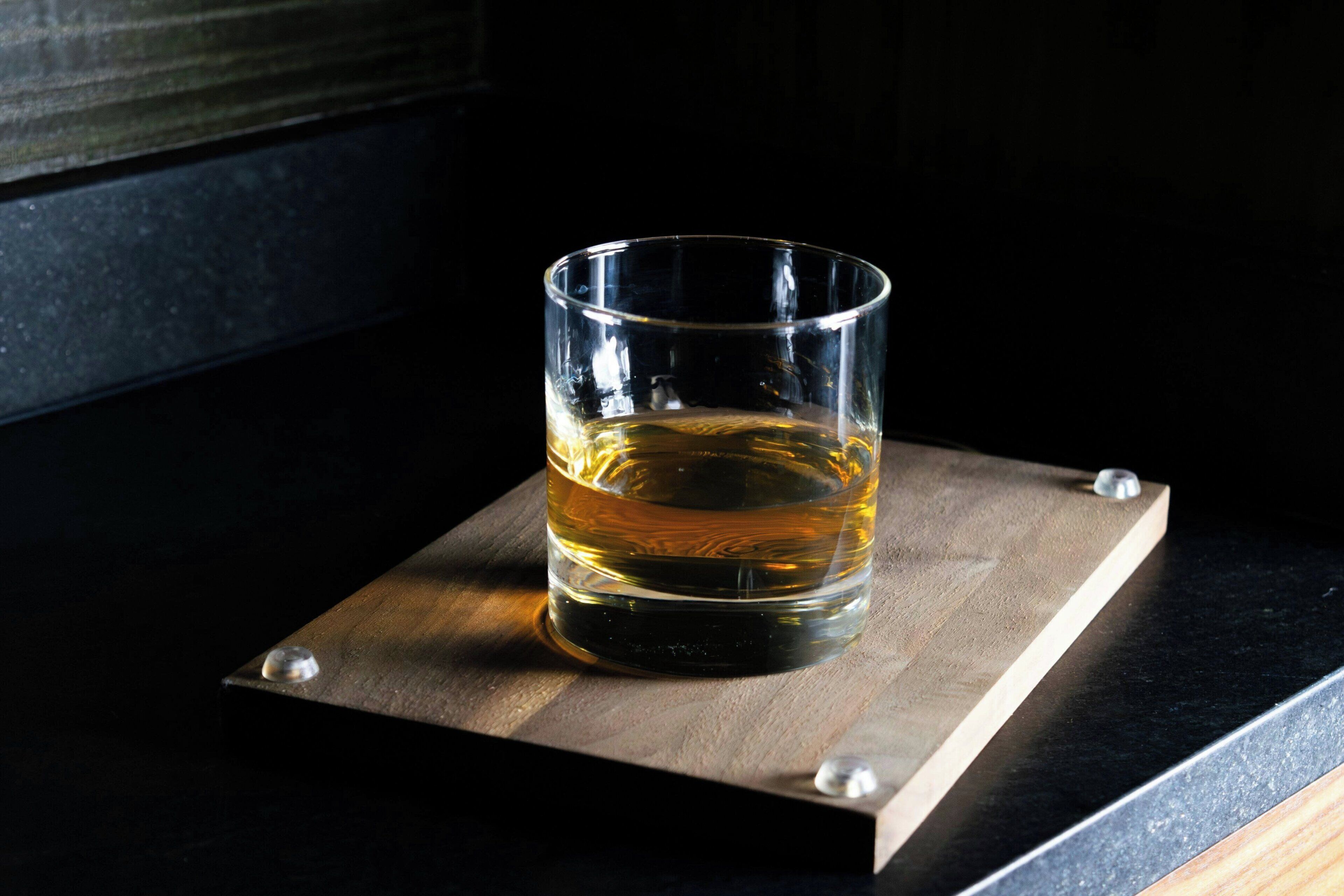 Un vaso de líquido ámbar sobre un posavasos de madera con tornillos metálicos.